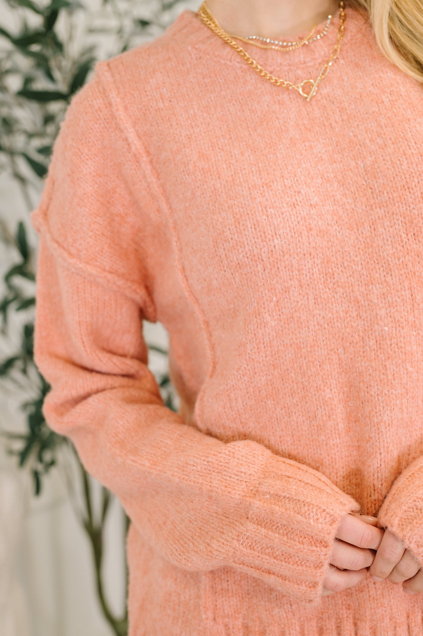 Person wearing a coral pink sweater with a blurred background