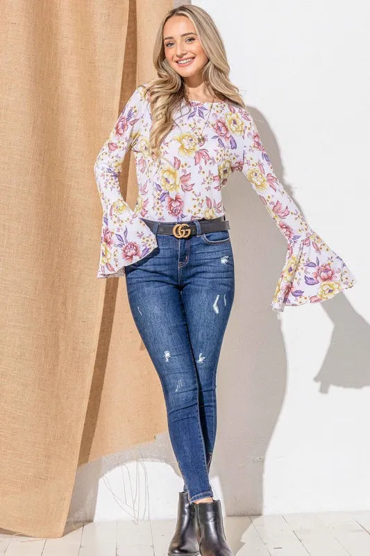Woman wearing a floral blouse and blue jeans standing against a neutral background