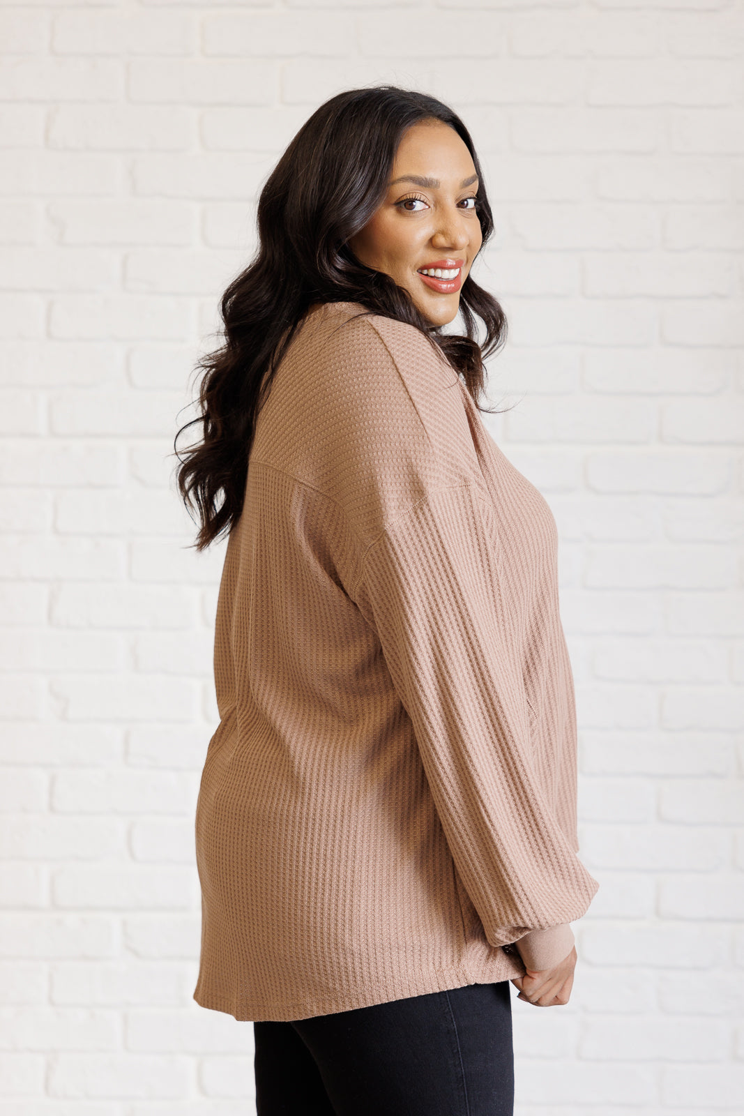 Woman wearing a beige ribbed sweater against a white brick wall