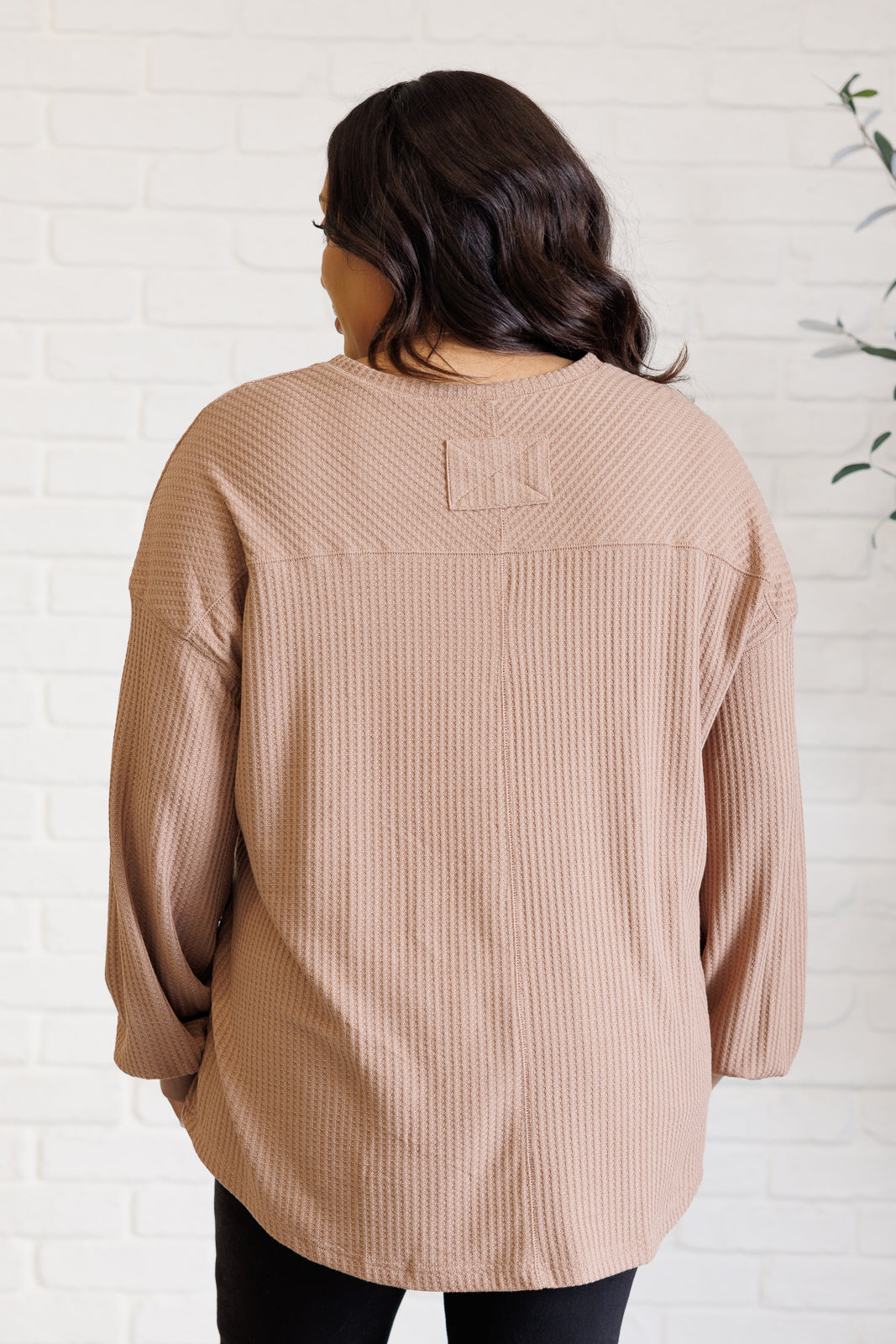 Person wearing a beige ribbed sweater against a white brick wall.