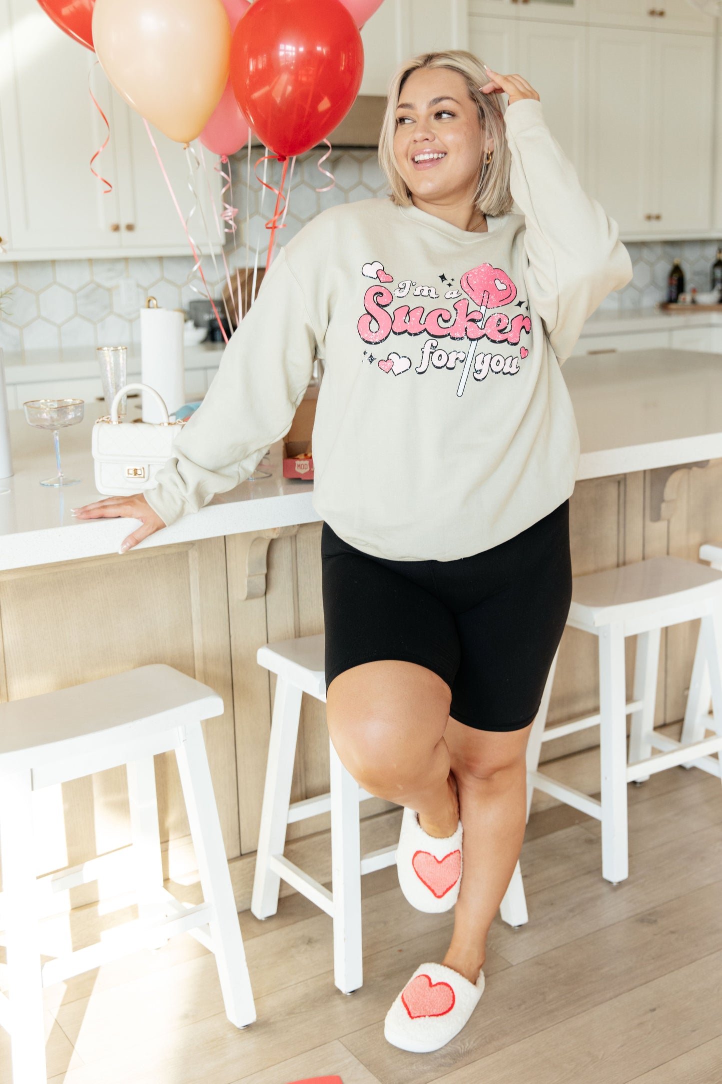 a woman wearing matching valentines "Ima sucker for you" pullover in a living room.