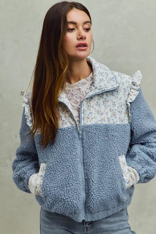Woman wearing a blue fleece sherpa jacket with floral patterns on a neutral background